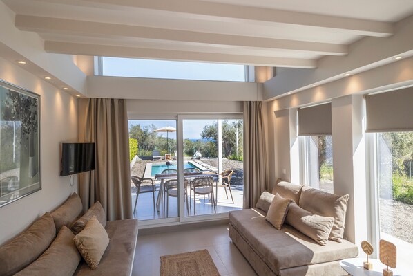 A modern living room with a sofa, a TV, and a view of an outdoor pool area.