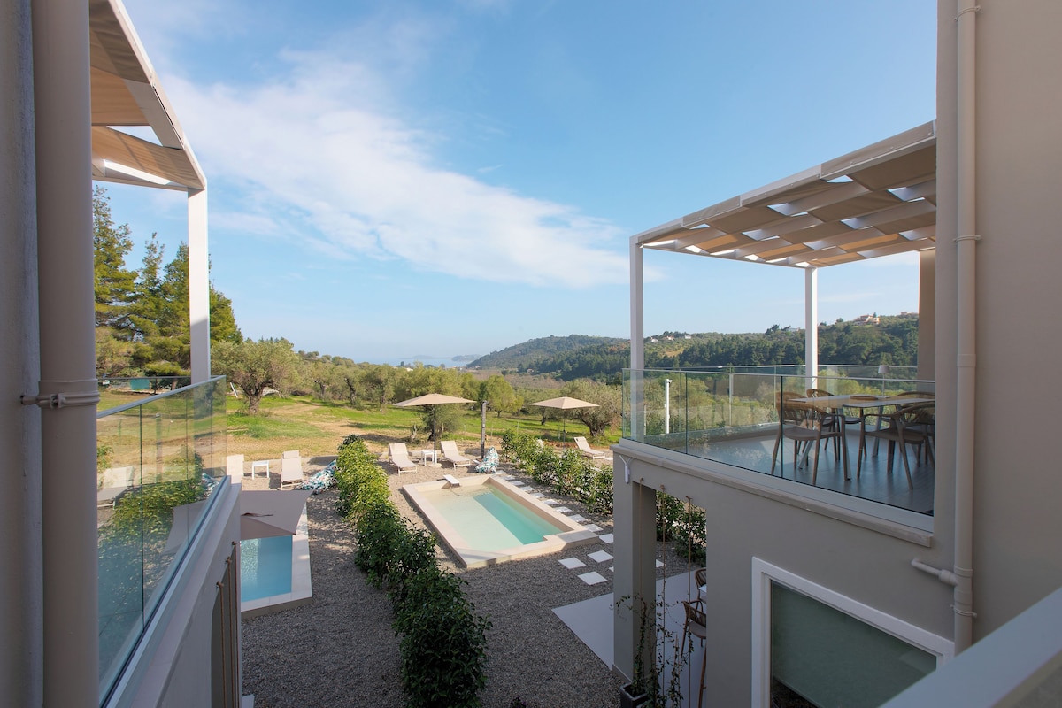 A balcony with a pool, lounge chairs, and a view of the countryside.