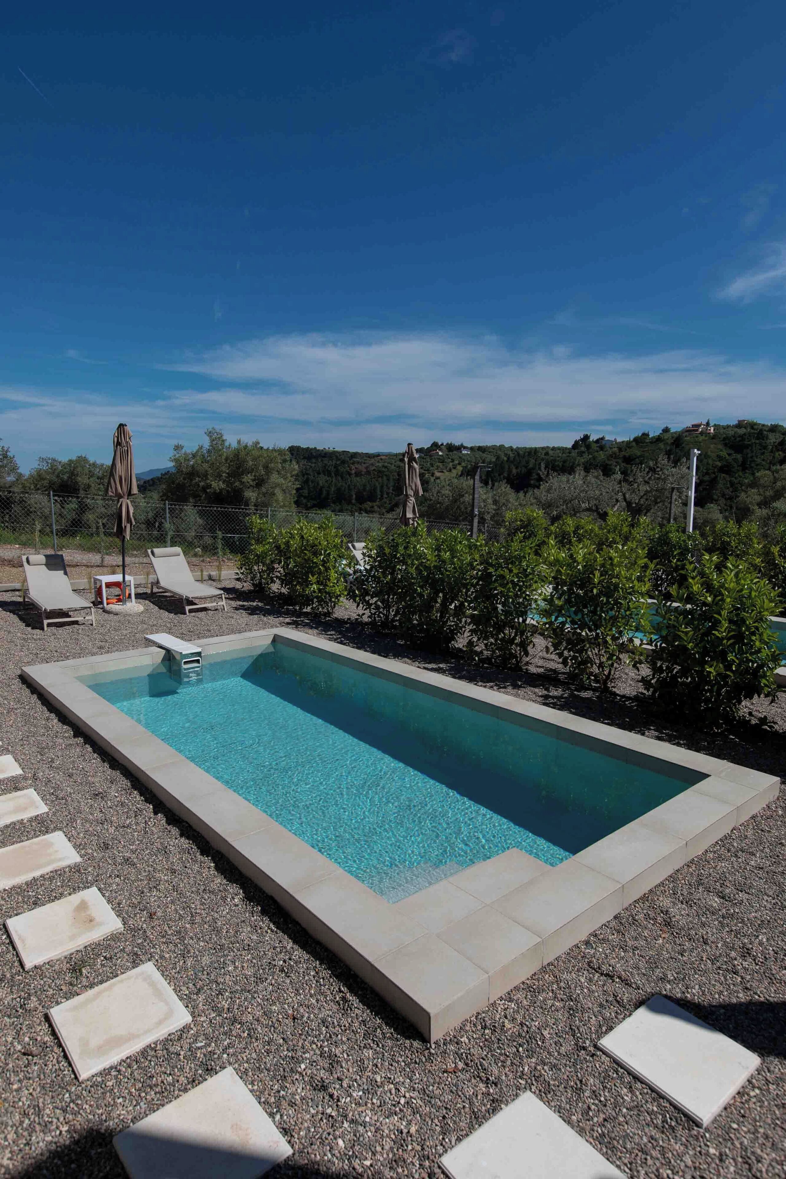 A rectangular swimming pool with a clear blue water, surrounded by a gravel area with stepping stones.