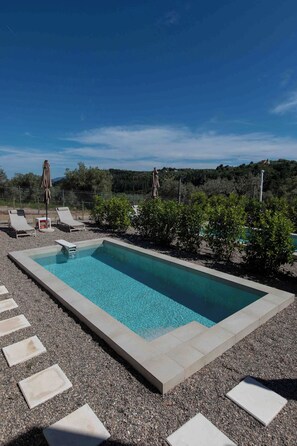 Une piscine rectangulaire à l’eau d’un bleu limpide, entourée d’une zone recouverte de gravier et agrémentée de pas japonais.