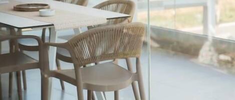 A modern outdoor dining area with glass railings, wicker chairs, and a view of the surrounding landscape.