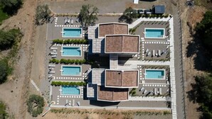 An aerial view of a resort with multiple swimming pools, arranged in a grid pattern, surrounded by lounge areas and vegetation. - KAELA Pool Villas (Agios Nikolaos)
