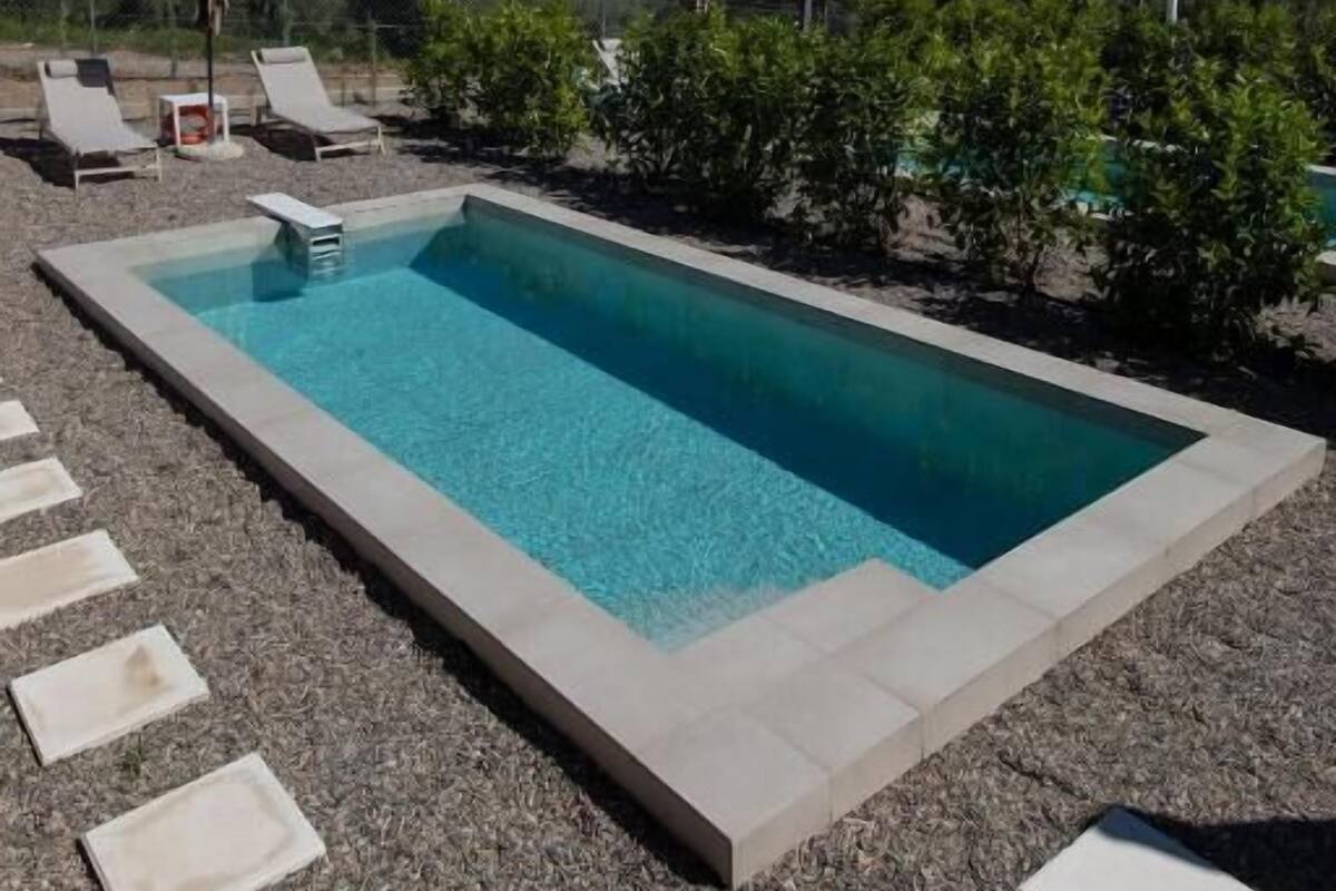 Piscina rectangular con agua azul cristalina, rodeada por una zona de grava y baldosas blancas.