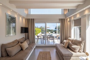 A spacious living area with two sofas, a flat-screen TV, and a large sliding glass door leading to an outdoor patio with a pool.