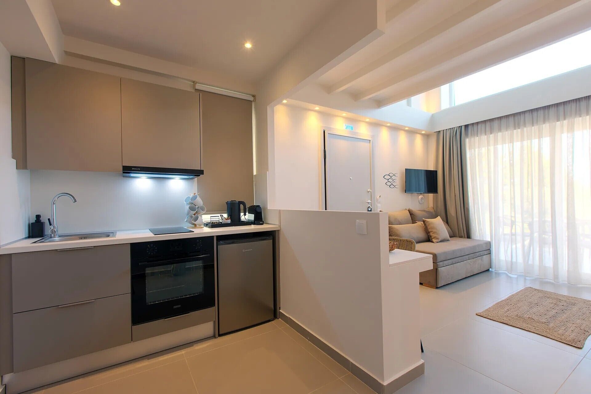 A modern kitchen with built-in appliances, a dining area with a sofa, and a TV mounted on the wall.