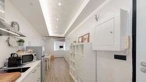 Una cocina moderna con microondas, hervidor y tetera sobre la encimera. Se observa un armario blanco con estantes en la pared.