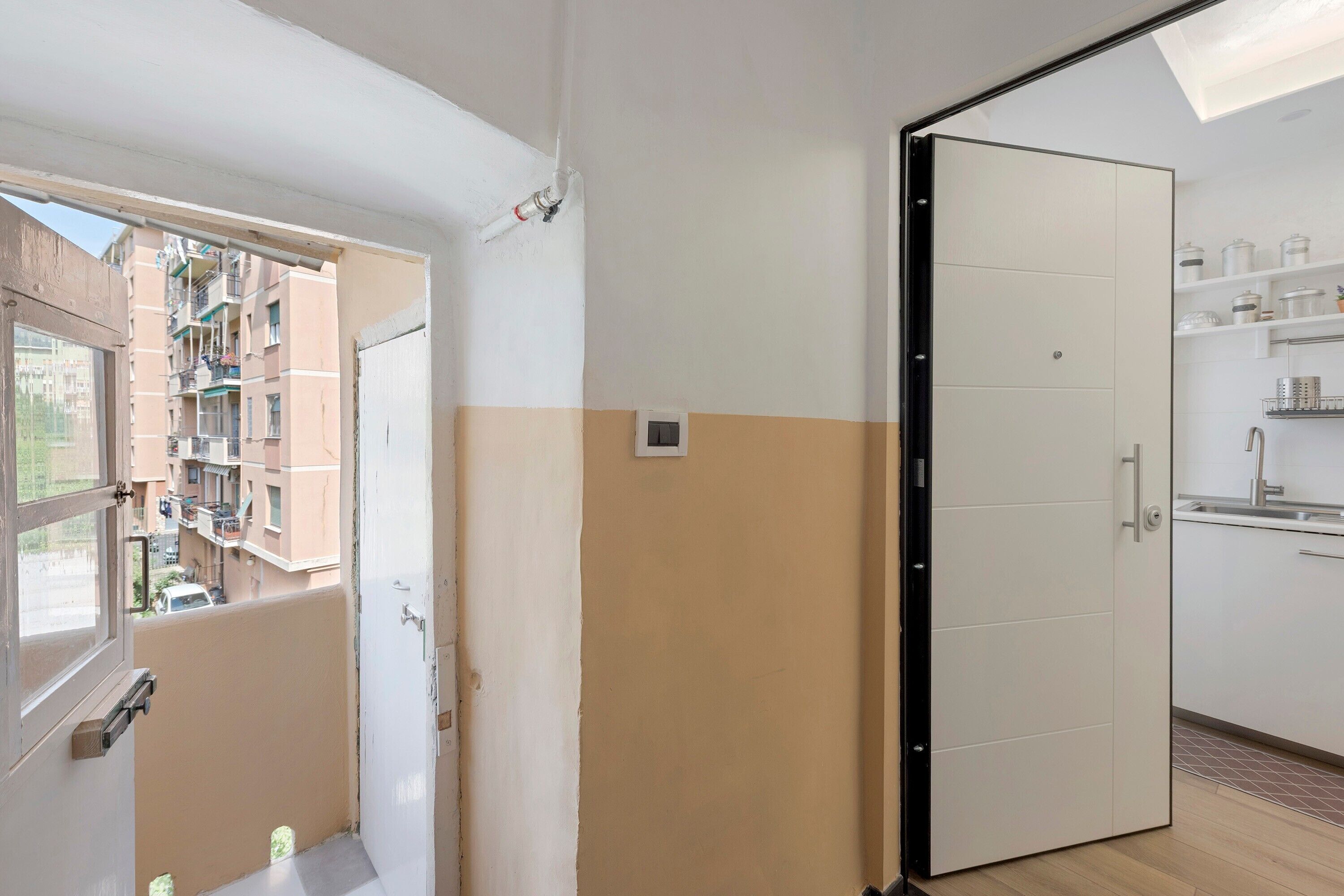 Ein Zimmer mit Schiebetür, einem Fenster mit Balkonblick und einer Küchenzeile inklusive Schränken und Arbeitsfläche.
