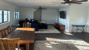 A spacious living area with a wooden dining table, a sofa, a TV mounted on the wall, and ceiling fans. - Waterfront Studio minutes from Downtown Annapolis and Naval Academy (Edgewater)