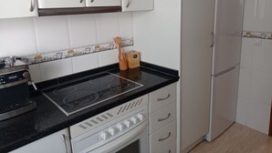 Une cuisine avec des armoires blanches, un plan de travail noir, une cuisinière et un réfrigérateur.