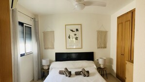 Une chambre d’hôtel avec un lit, un ventilateur de plafond, un tableau encadré au mur et une armoire en bois.