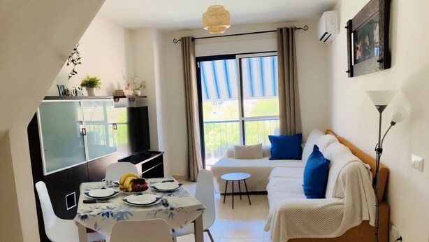Un coin repas avec une table dressée pour deux personnes, un canapé et un téléviseur.