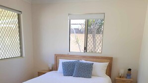 A bedroom with a wooden bed, two bedside tables, a woven rug, and a window with a view. - Enjoy a relaxing stay at this cosy one bedroom granny flat near the sea (Warnbro)