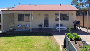 A single-story house with a covered porch, a barbecue grill, and a fenced yard. - Enjoy a relaxing stay at this cosy one bedroom granny flat near the sea (Warnbro)