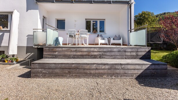 Ein zweistöckiges Gebäude mit einer Holztreppe, die zu einem Balkon mit Gartenmöbeln führt.