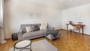 Ein modernes Wohnzimmer mit einem grauen Sofa, einem Holztisch und einem weißen Stuhl.