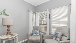 A corner room with two beige armchairs, a small table with a lamp, and a butterfly decoration on the wall. - 7 Bedrooms-OceanLakes-Sleeps18-GolfCart Included (Myrtle Beach)