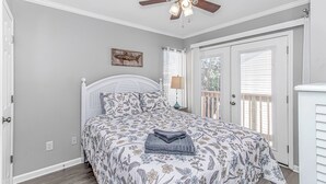 A bedroom with a bed, a ceiling fan, a nightstand, a lamp, a window with blinds, and a door. - 7 Bedrooms-OceanLakes-Sleeps18-GolfCart Included (Myrtle Beach)