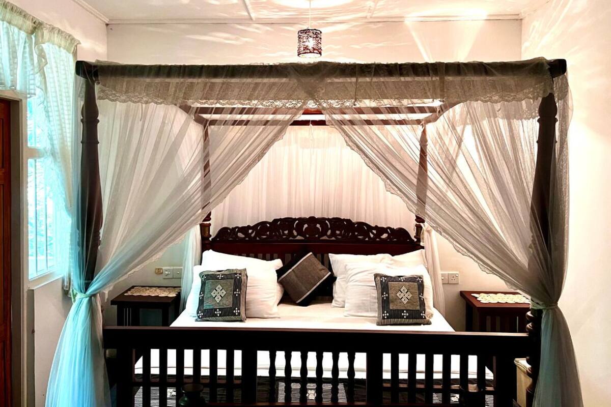 A four-poster canopy bed with a wooden headboard, two bedside tables, and a nightstand.