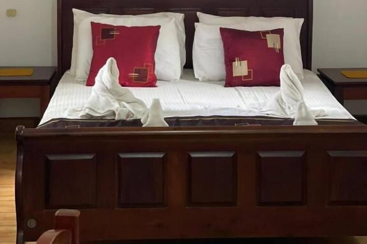 A neatly made bed with white and red pillows, a hanging robe, and wooden headboard.