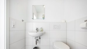 Un baño con lavamanos blanco, espejo, inodoro y cubo de basura.