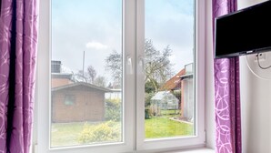 Una habitación con ventana, un televisor montado en la pared y un control remoto en el alféizar.