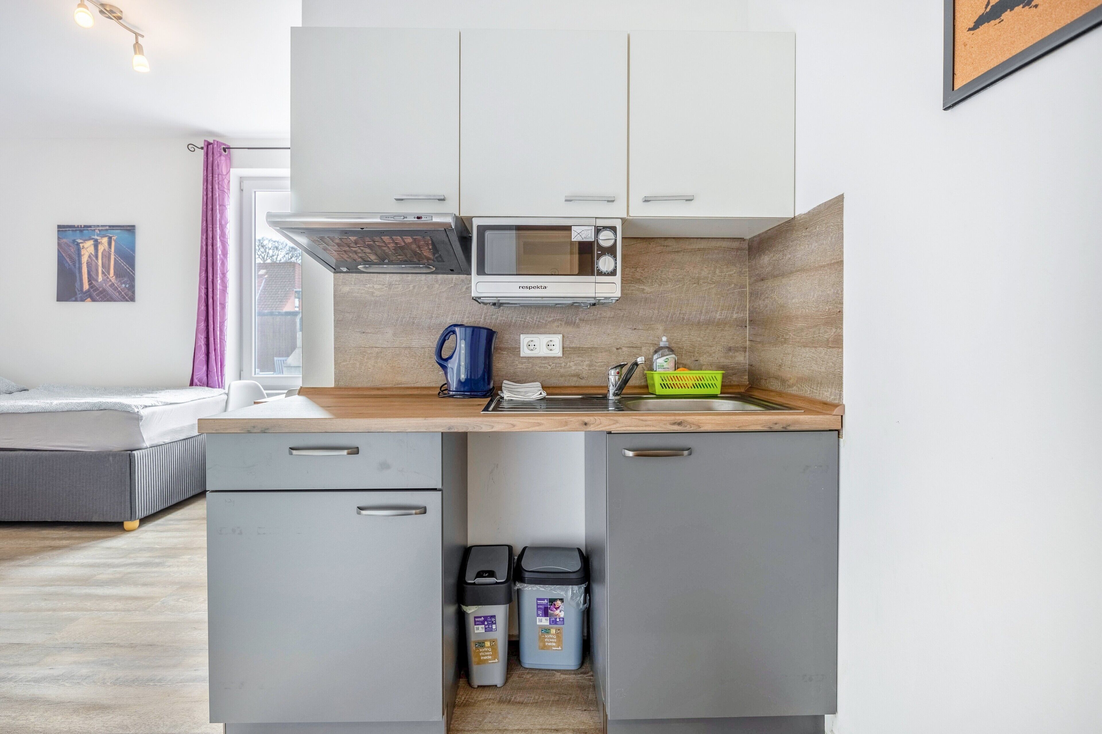 A compact kitchen with a microwave, sink, and two trash bins.