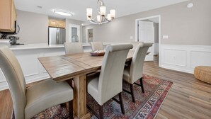 Un comedor con una mesa y sillas de madera, un candelabro y una cocina al fondo.