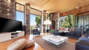 A modern living room with a stone wall, wooden ceiling, a flat-screen TV, a white coffee table, and two sofas. - AGROLUX OASIS - A Private Pool Escape in Lush Agricultural Serenity (Rhodes)