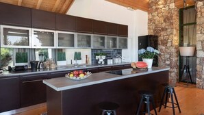 A modern kitchen with a central island, bar stools, and a stone accent wall. - AGROLUX OASIS - A Private Pool Escape in Lush Agricultural Serenity (Rhodes)
