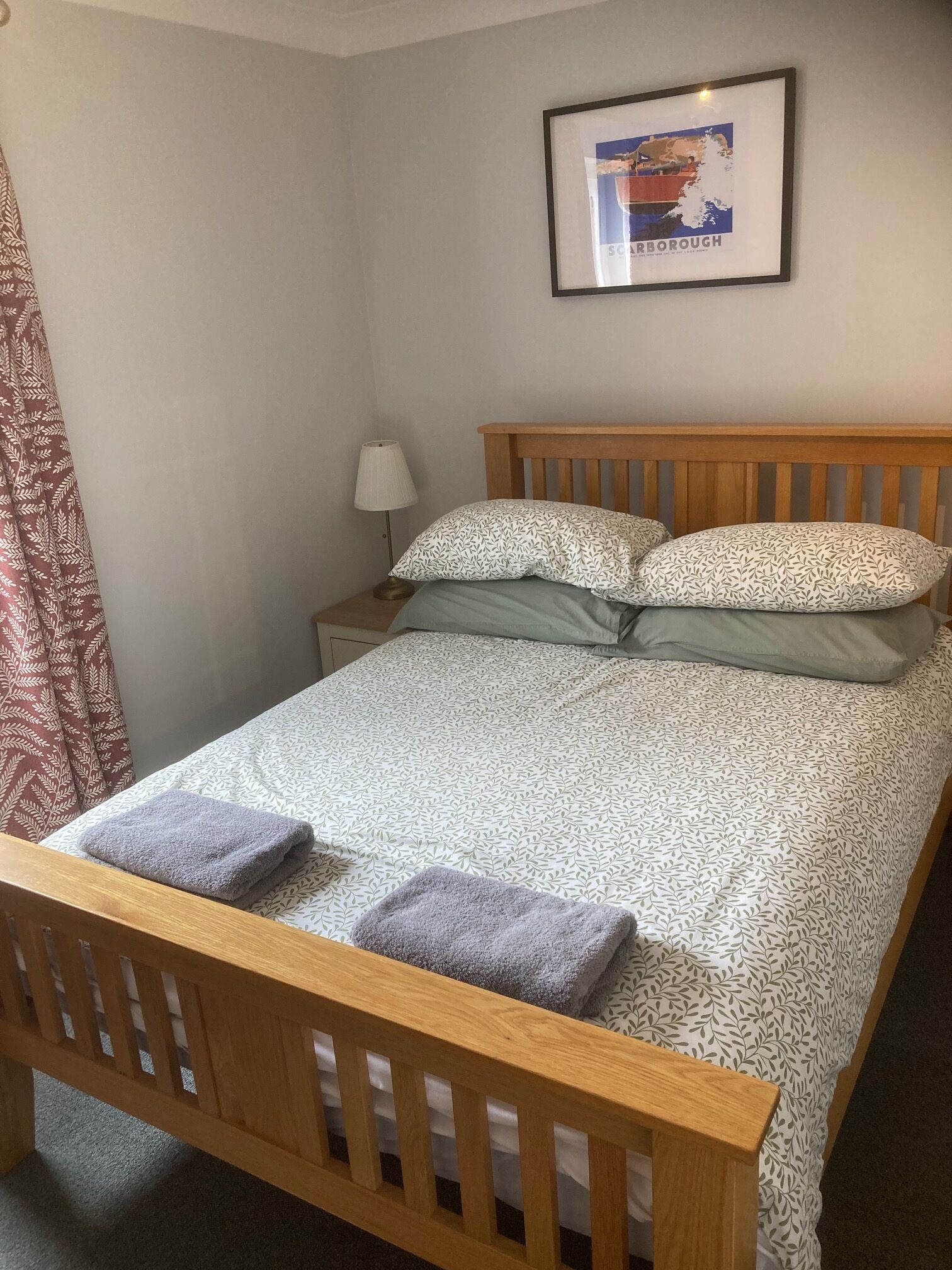 A single bed with a patterned bedspread, two pillows, a nightstand with a lamp, and a framed picture on the wall.
