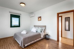 A bedroom with a bed, a window, an air conditioning unit, a framed picture, and a door. - A spacious villa w/private pool - 10 ride min from the beach, center & old town! (Rhodes)