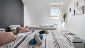 Une chambre moderne avec un plafond en pente, une lucarne, un lit avec une literie à motifs, une table de chevet et une étagère murale agrémentée d’une plante.