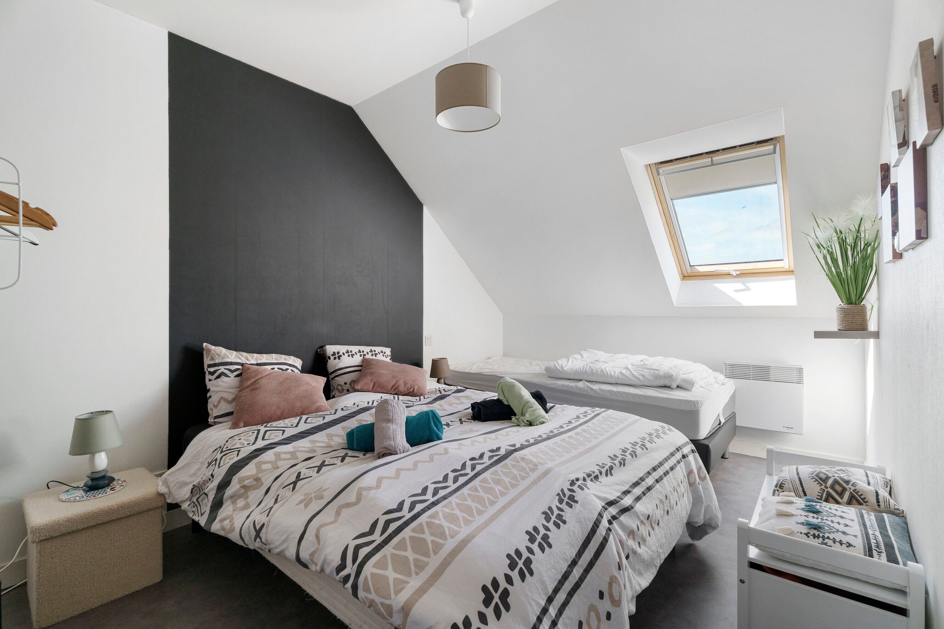 Um quarto moderno com teto inclinado, uma cama com roupa de cama estampada, uma mesa de cabeceira com abajur e uma janela com vista.