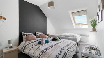 Um quarto moderno com teto inclinado, uma cama com roupa de cama estampada, uma mesa de cabeceira com abajur e uma janela com vista.
