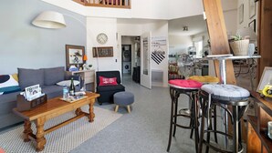 Un vaste espace de vie doté d’un haut plafond, d’un escalier en bois, d’un canapé, d’une table basse et d’une cuisine à l’arrière-plan.