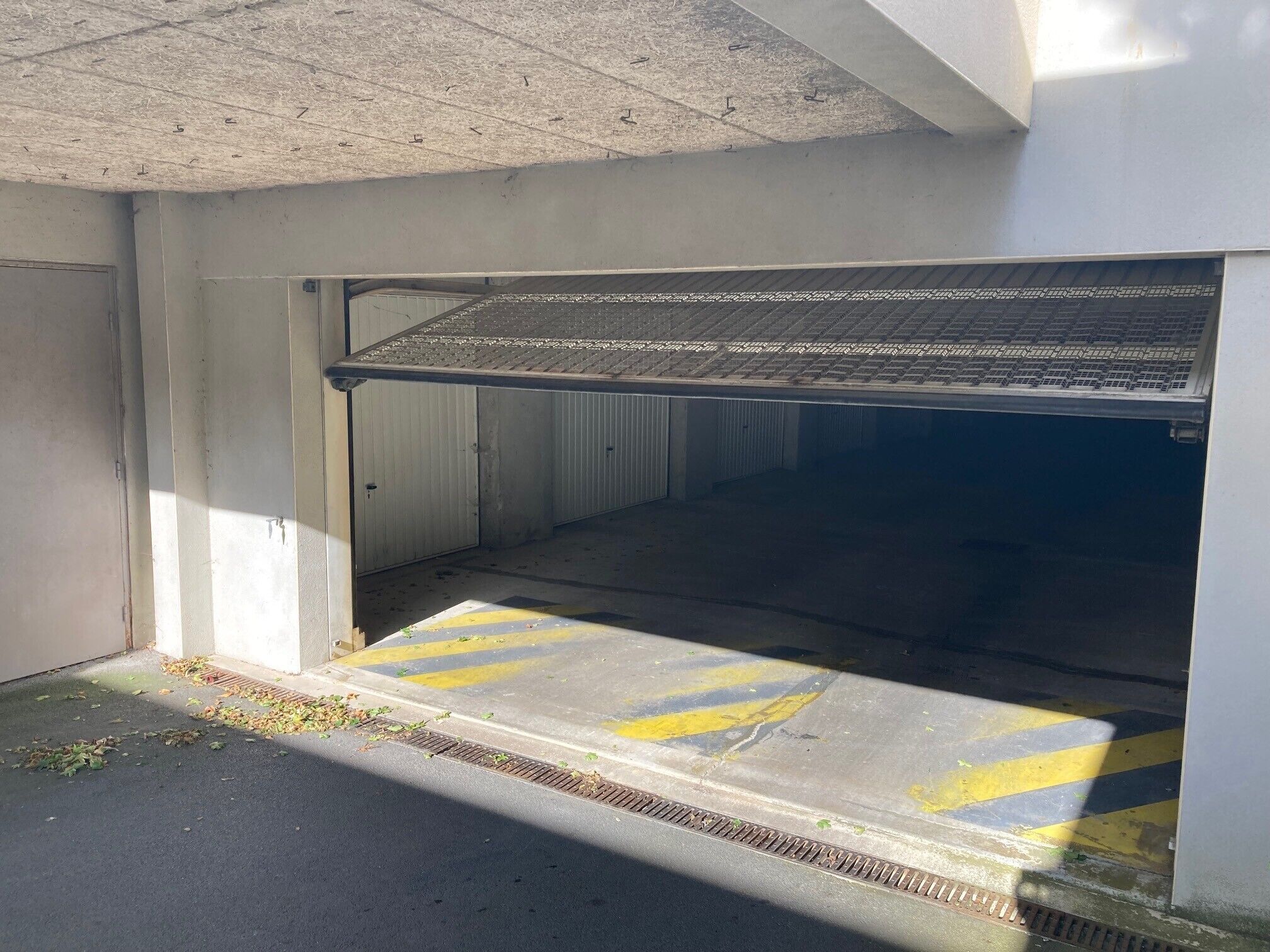 Une entrée de garage avec une rampe métallique menant à une zone abritée.