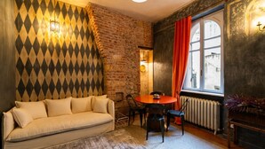A cozy room with a sofa, a round table, chairs, a brick wall, a window with curtains, and a radiator. - Historic and elegant Catullo residence (Verona)