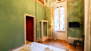 A hotel room with two beds, a TV, a chandelier, a window, and a door. - Historic and elegant Catullo residence (Verona)