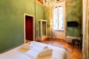 Ein Hotelzimmer mit zwei Betten, einem Fernseher, einer Chandelüster, einem Fenster und einer Tür.