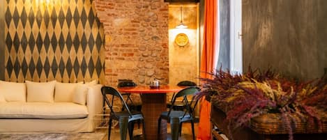 A cozy room with a brick wall, a patterned wall, a sofa, a table with chairs, and a decorative plant.