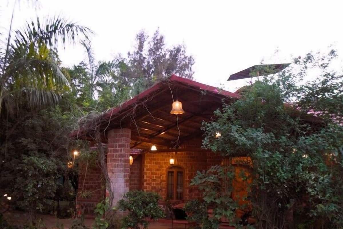 Una casa de ladrillo rústica con techo rojo, rodeada de abundante vegetación y un césped cuidado.