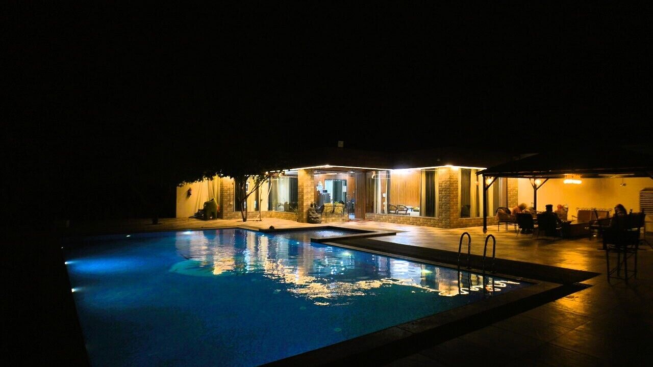 Ett område med en pool som är öppet på kvällen, med en byggnad, utomhusmöbler och en täckt uteplats.