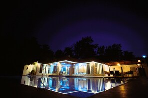 Ein Haus mit Swimmingpool bei Nacht, beleuchtet von Lichtern.
