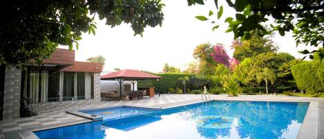 A swimming pool with a patio area, a gazebo, and a view of a house with a red roof.