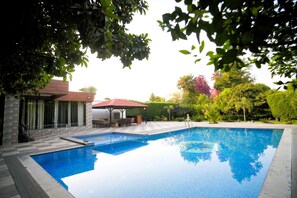 A swimming pool with a patio area, a gazebo, and a view of a house with a red roof. - The Mannat Farms (Taoru)