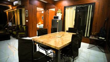 Una habitación con pared de paneles de madera, una mesa de comedor con sillas, un refrigerador, una guitarra y un ventanal con cortinas.