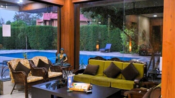 A modern living room with a pool view, wooden ceiling beams, and a ceiling fan. - The Mannat Farms (Taoru)