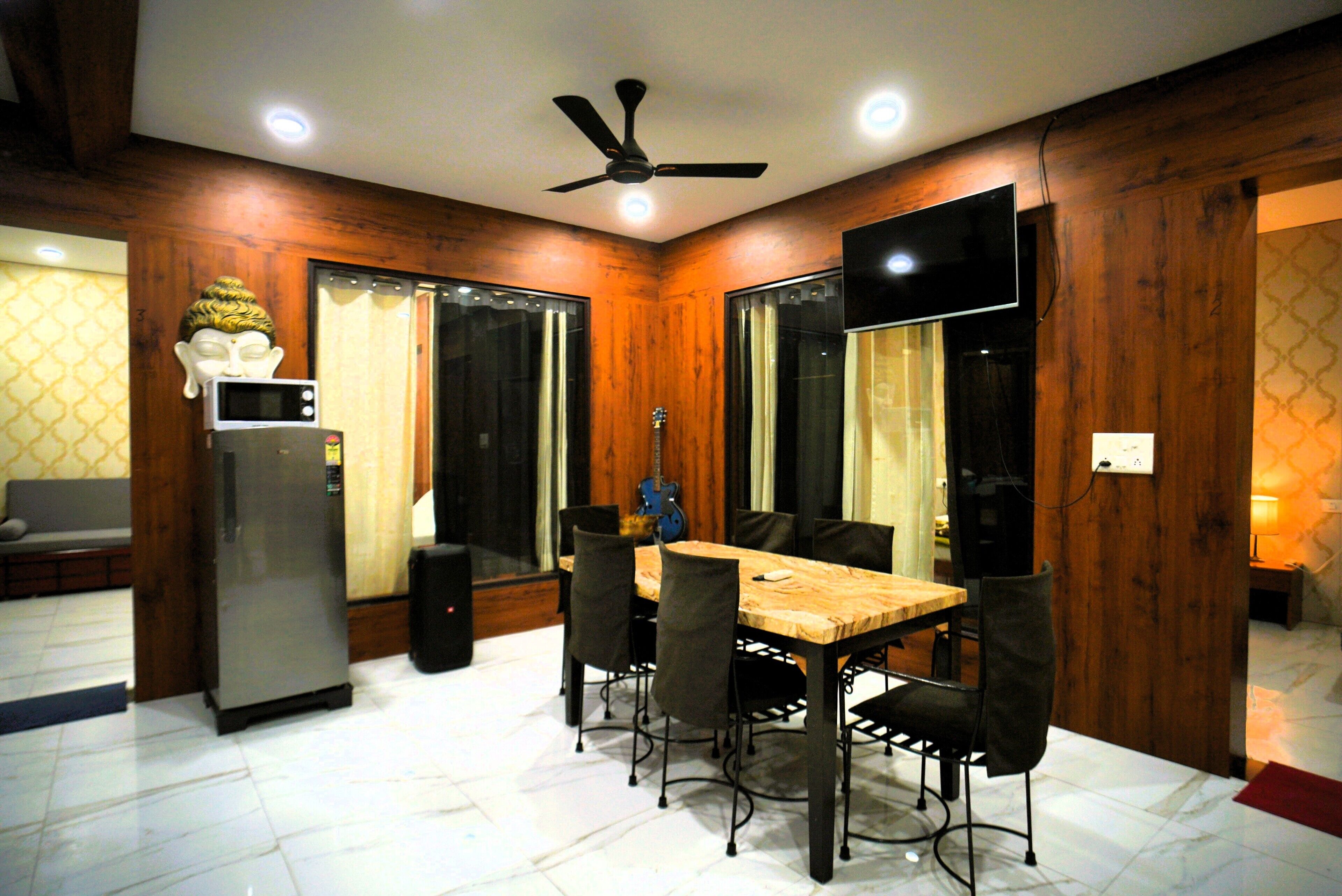 A dining area with a wooden table and chairs, a ceiling fan, and a television mounted on the wall.