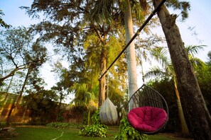 Eine Hängestuhl-Sitzgelegenheit, die zwischen Bäumen in einem Garten hängt, mit einer Rasenfläche und einer Ziegelmauer im Hintergrund.