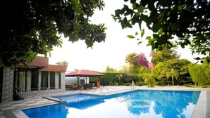 A swimming pool with a patio area, a gazebo, and a view of a house with a red roof. - The Mannat Farms (Taoru)